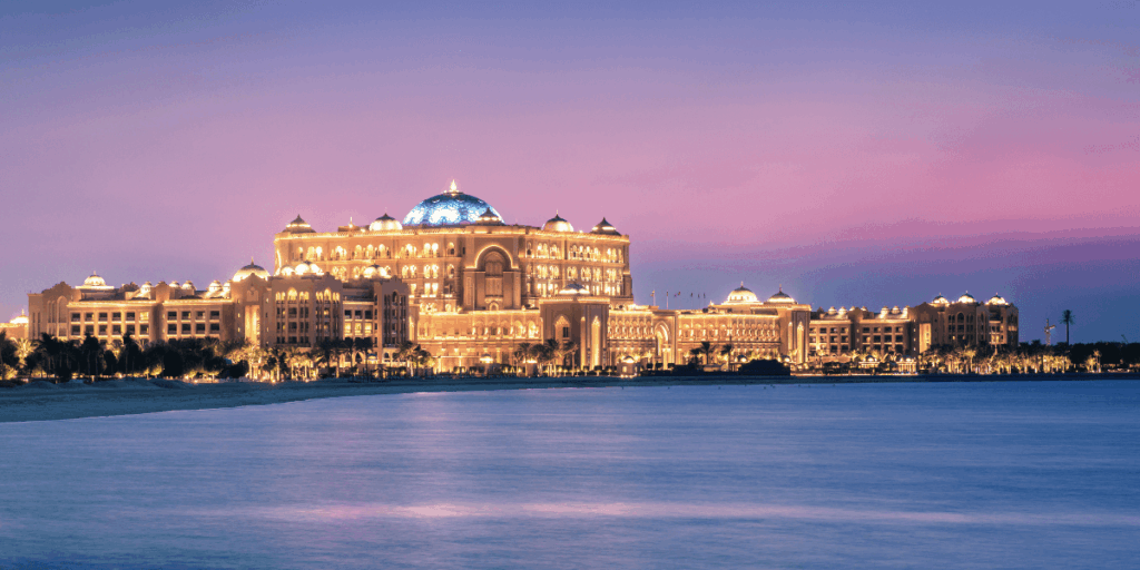 圖中可見著名的 Emirates Palace，在夕陽後的藍紫色天幕下亮起金色燈光，建築奢華壯闊，配上海面反射的柔和光線，營造華麗卻寧靜的氛圍，是阿布達比最具代表性的豪華地標之一。
