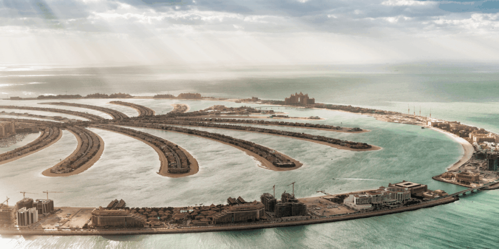 由高空俯瞰著名的棕櫚島（Palm Jumeirah），人工島呈現棕櫚樹形狀延伸入海，遠方可見亞特蘭提斯飯店。這張照片展現了杜拜的建築奇蹟與現代奢華的象徵。